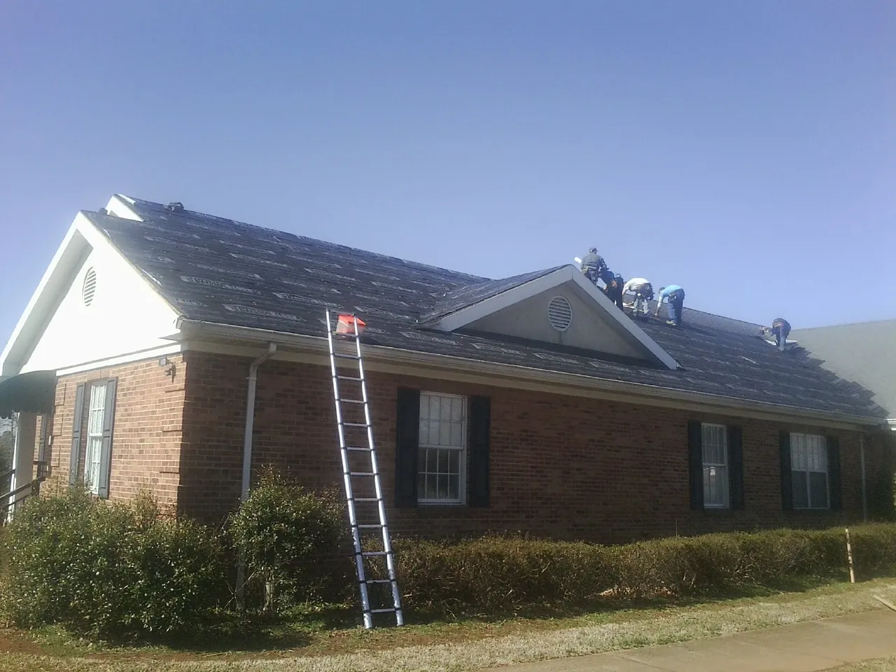 Crew tearing shingles off a brick ranch roof with a ladder set — Emergency Roof Repair work by our crew in West Dennis