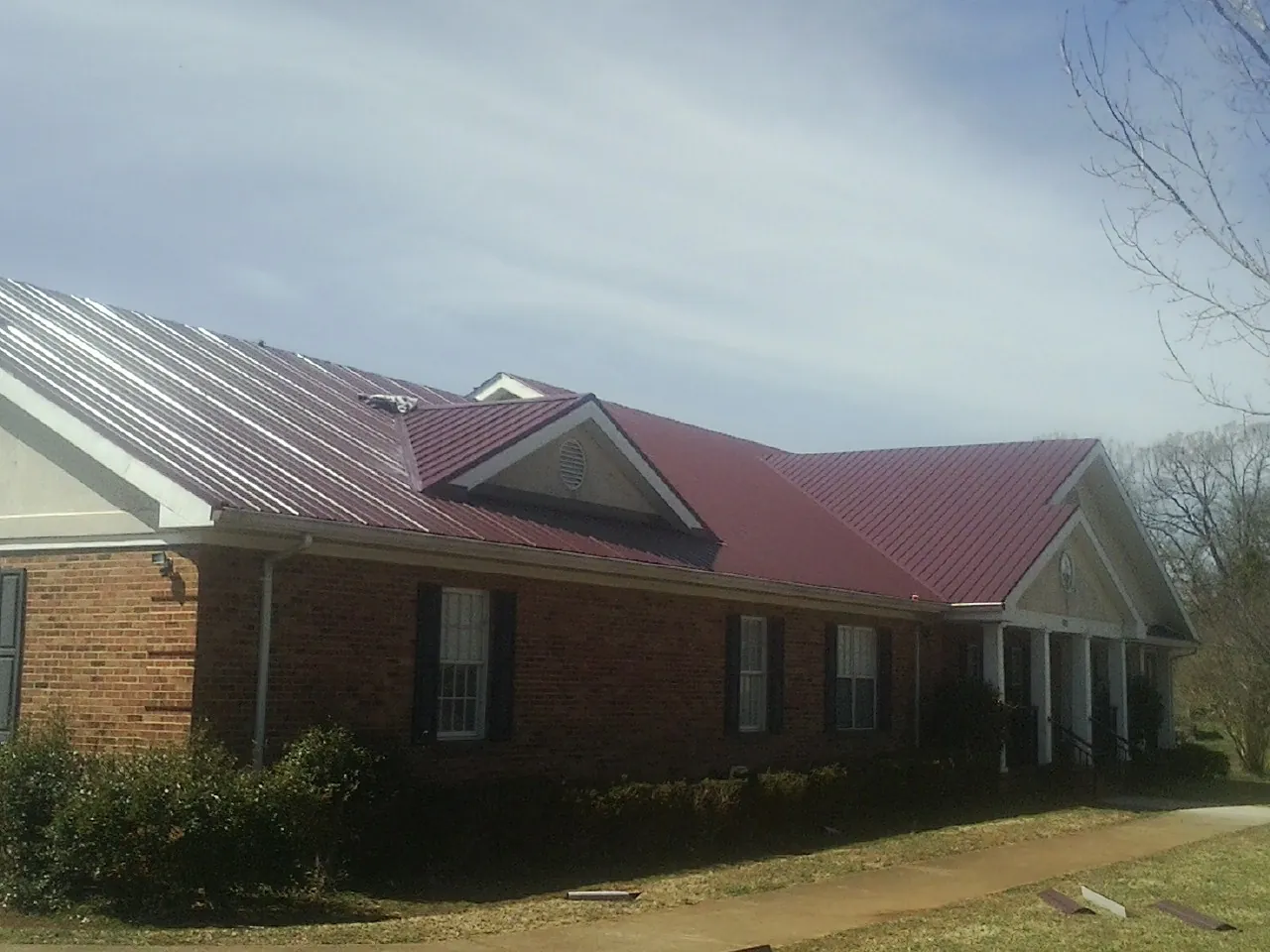 Red metal roof with gabled entries on a long brick building, from a Hail Damage Roof Repair job in West Dennis