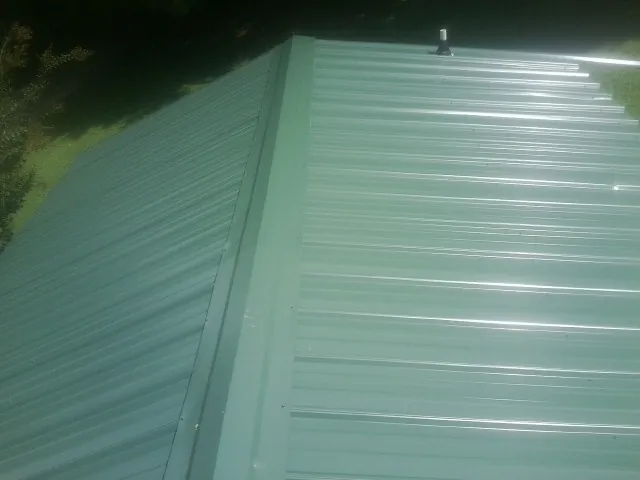 New green metal panels meeting at the ridge of a roof — Flat Roof Repair work by our crew in West Dennis