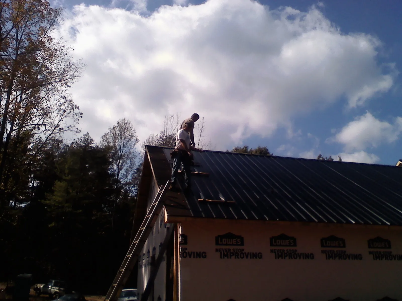 Roofer fastening dark metal panels high against a cloudy sky, from a Roof Inspection job in West Dennis