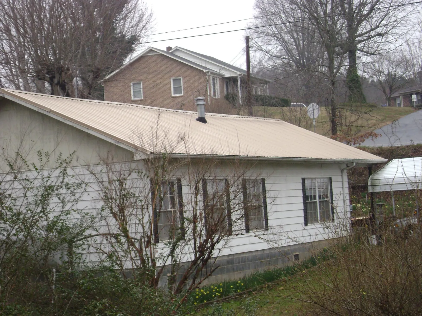 Tan metal roof on a white sided house set into a hillside — Commercial Roofing by Roofing Brothers in West Dennis